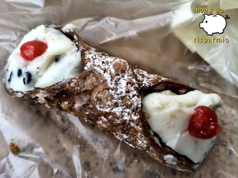 Tradizionale cannolo siciliano con cialda fritta croccante spolverata di zucchero a velo, farcito con crema di ricotta, gocce di cioccolato e ciliegie candite alle estremità