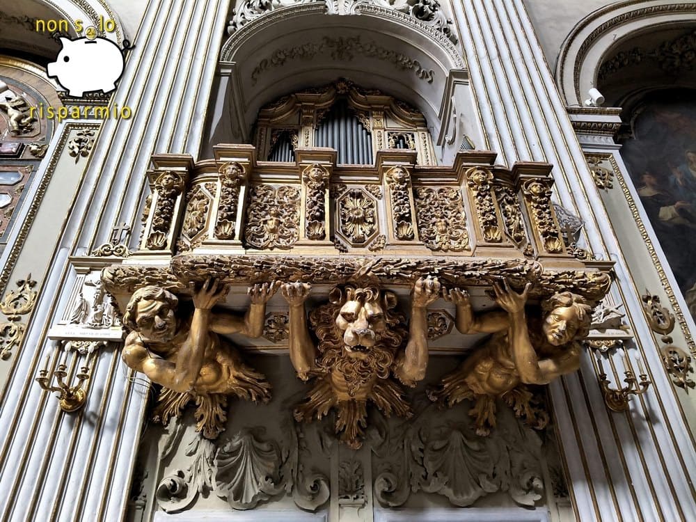 Pregevole cantoria lignea dorata d'epoca barocca sostenuta da imponenti figure scolpite di atlanti e una testa di leone, posta sotto le canne dell'organo di una chiesa