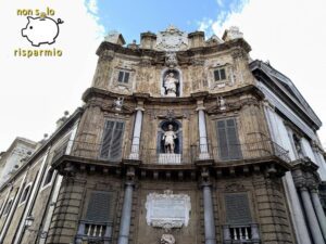 Vista prospettica dal basso della facciata barocca dei Quattro Canti a Palermo affiancata da un edificio adiacente, sotto un cielo azzurro con nuvole.